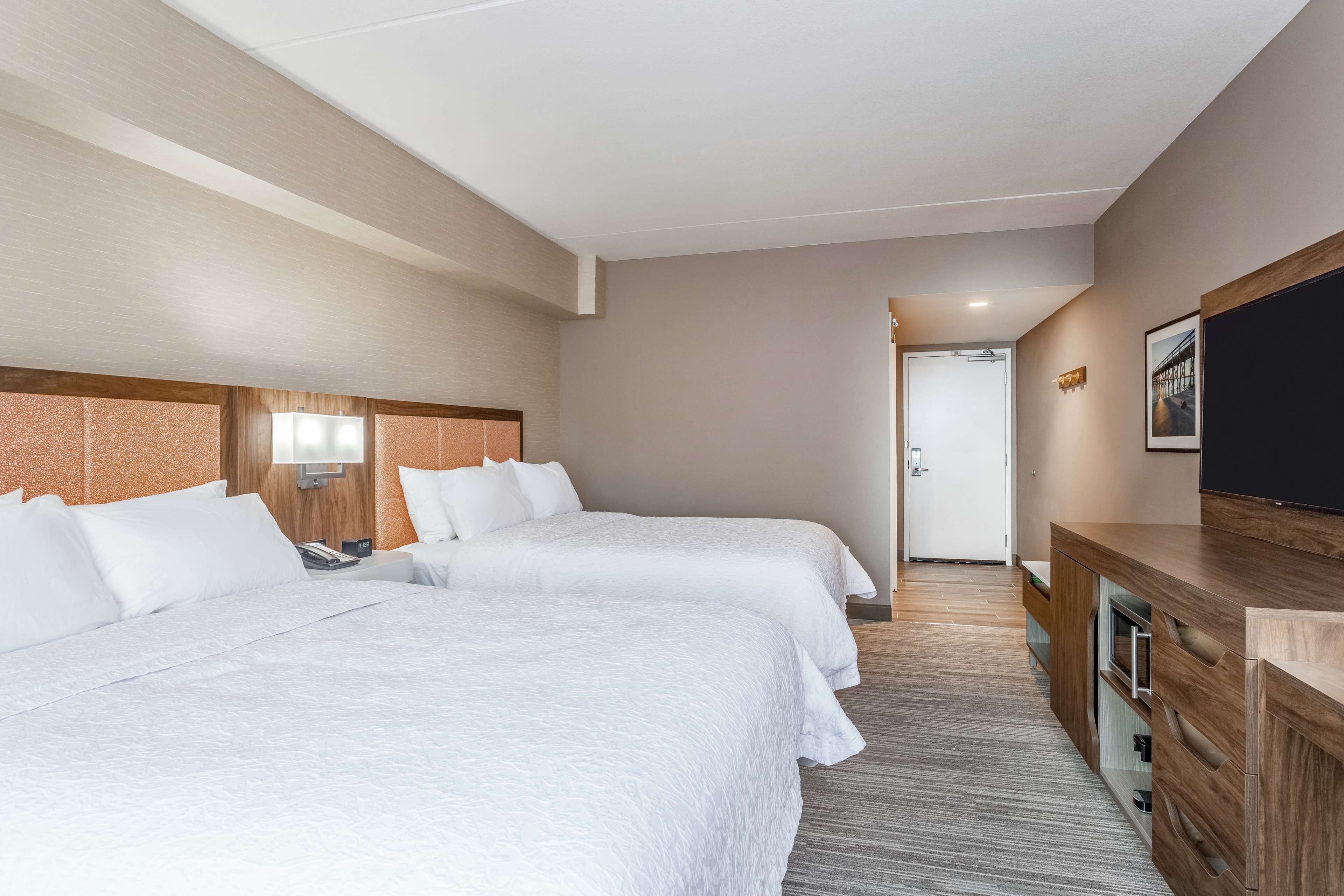 A hotel room with two beds, a wooden dresser, a flat-screen TV, and a door leading to another room.