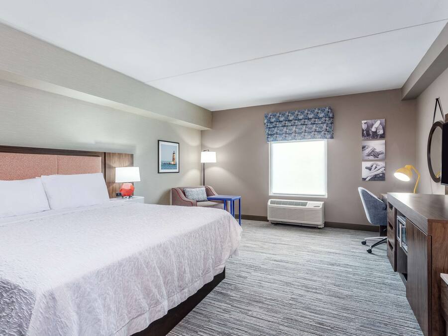 A hotel room with a large bed, a desk, a chair, a lamp, and a television.