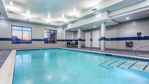 A swimming pool with clear blue water, surrounded by a tiled wall with blue accents, and a view of a sunset through large windows. - Hampton Inn & Suites Kittery-Portsmouth (Kittery)