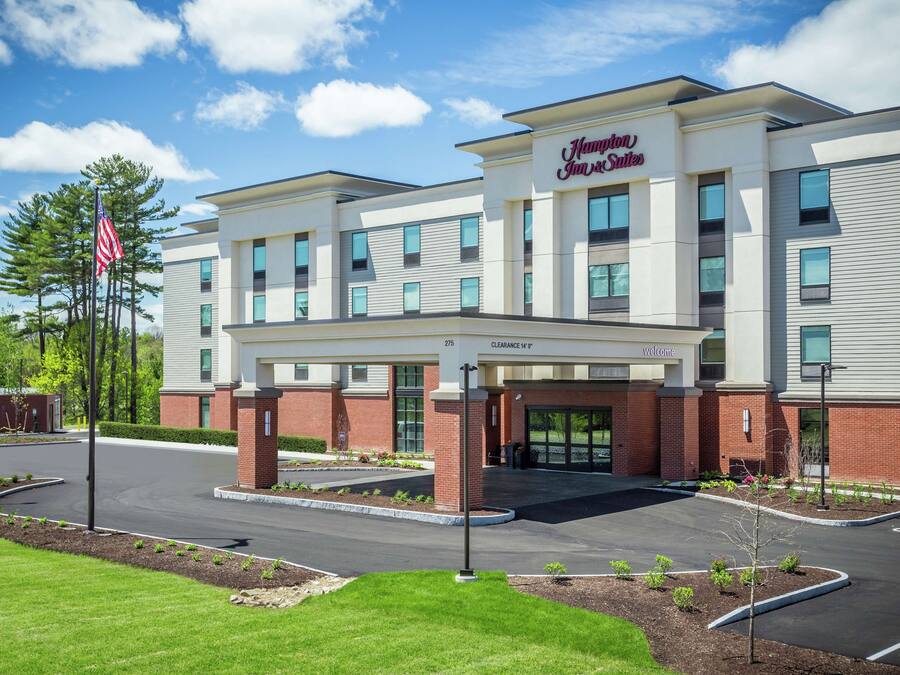 Un hotel Hampton Inn & Suites con un diseño moderno, que cuenta con una entrada despejada, un estacionamiento y un jardín delantero ajardinado.