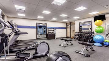 Un gimnasio con cintas de correr, elípticas, una prensa de banca, mancuernas y pelotas de ejercicio.
