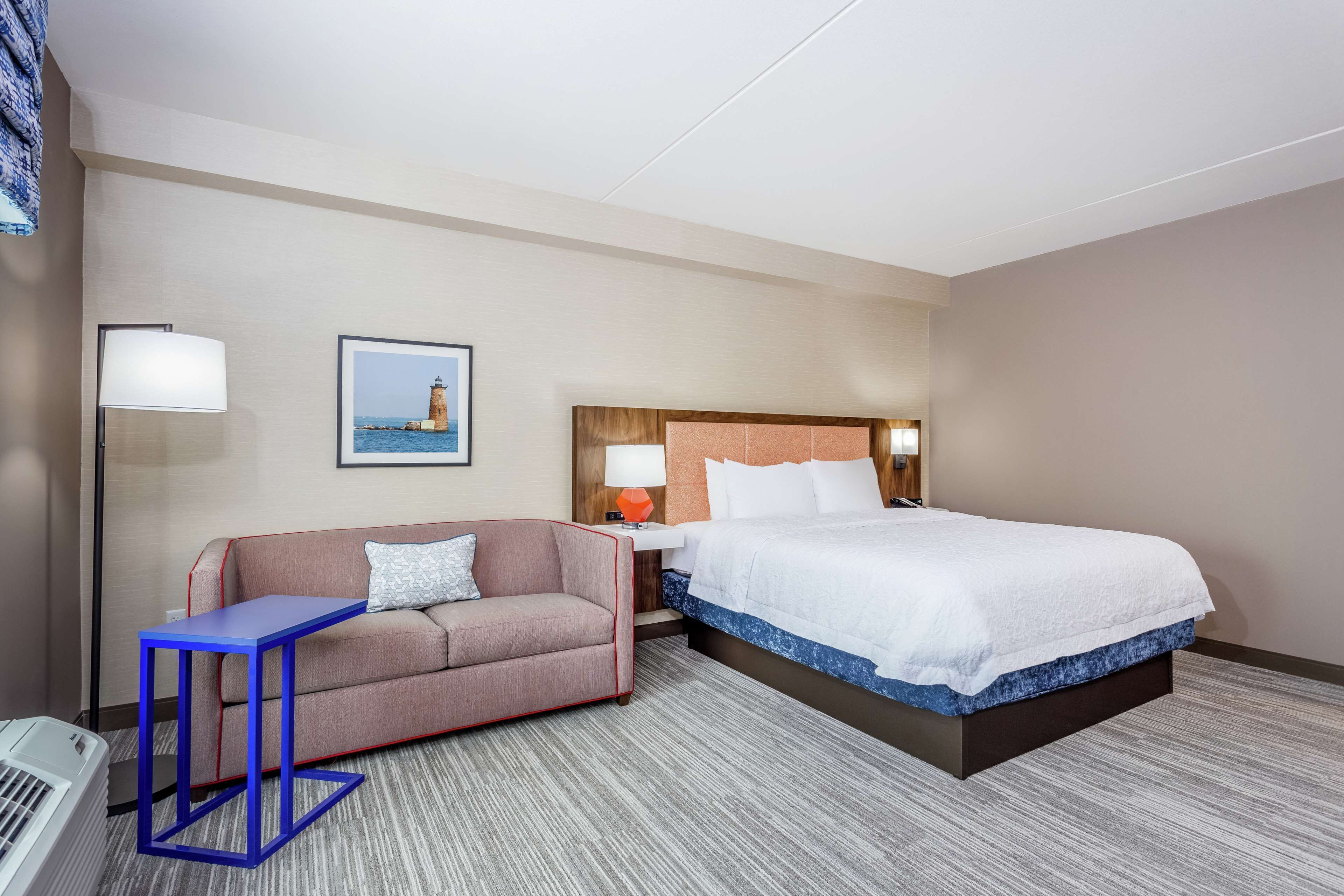 A hotel room with a bed, a sofa, a small table, a lamp, and a framed picture on the wall.