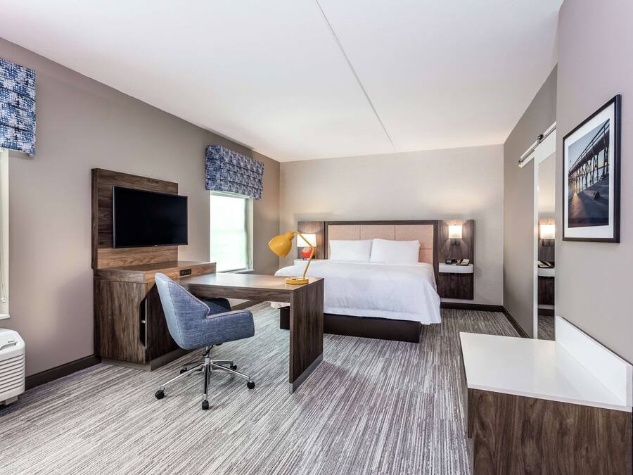 A hotel room with a bed, desk, chair, TV, and bedside lamps.