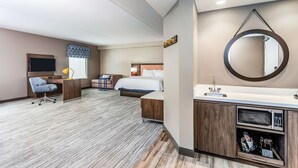 A hotel room with a bed, desk, chair, and a bathroom with a sink and mirror. - Hampton Inn & Suites Kittery-Portsmouth (Kittery)