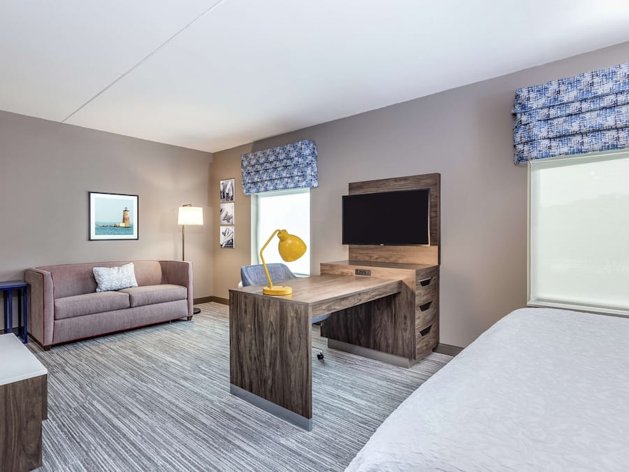 Et hotelværelse med sofa, skrivebord med lampe, tv og seng.