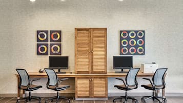 A conference room with a long table, four office chairs, two monitors, and wooden cabinets.