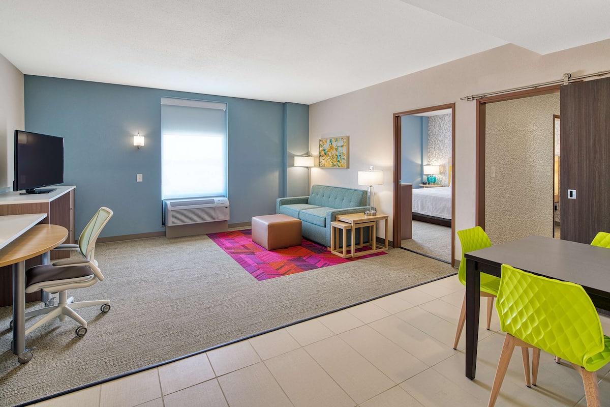 Une chambre d’hôtel moderne équipée d’un bureau, d’un fauteuil de bureau, d’un canapé et d’un coin repas avec des chaises.