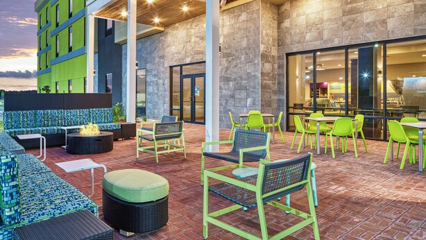 An outdoor patio area with seating and tables, a fire feature, and a view of the building's interior.