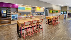 A modern cafe with wooden tables and red chairs, a counter with a coffee machine, and a refrigerated display.