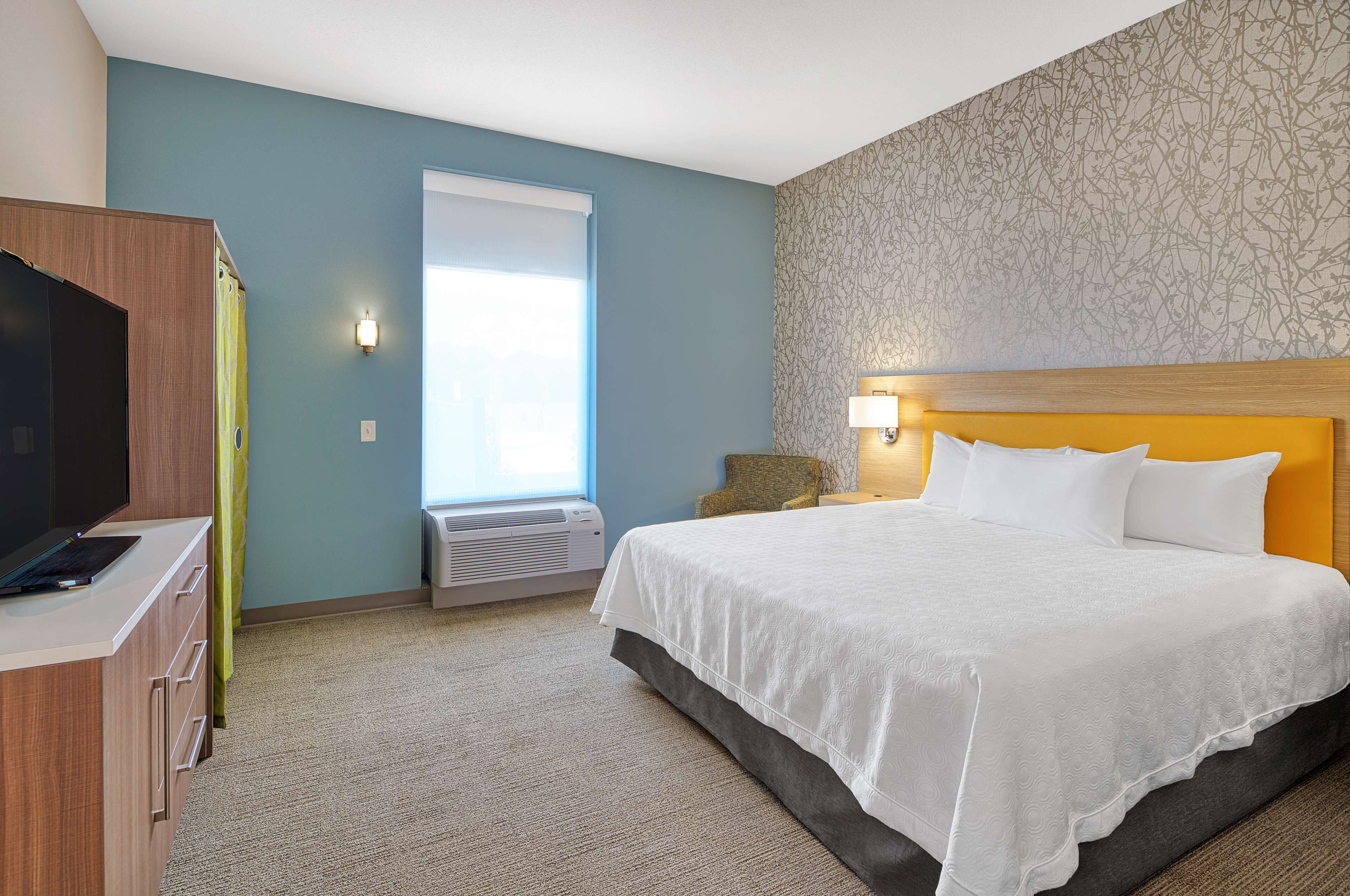 Une chambre d’hôtel avec un lit, un bureau, une télévision et une fenêtre avec des rideaux.