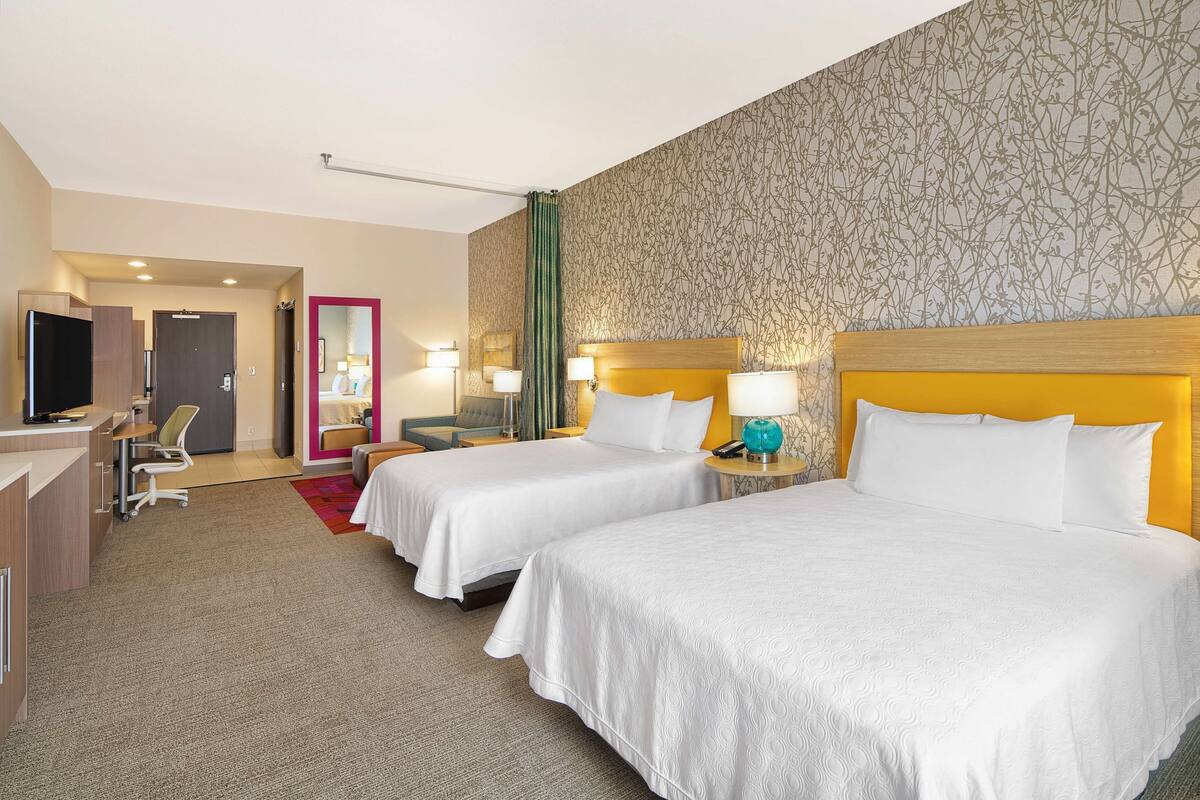 Une chambre d’hôtel avec deux lits, un bureau, une chaise et un téléviseur.