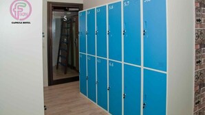 Pasillo de hotel con taquillas azules numeradas del 5.3 al 5.8, una puerta que da a una habitación y una pared con un cartel de ruta ciclista.