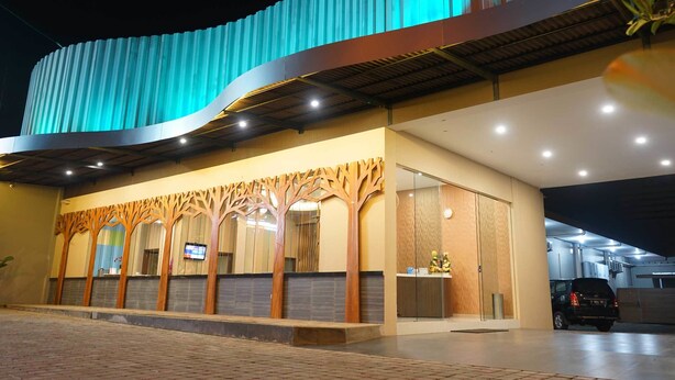 Un hotel moderno con fachada curva, un área de recepción con diseño de árbol en madera y un estacionamiento con un SUV negro.