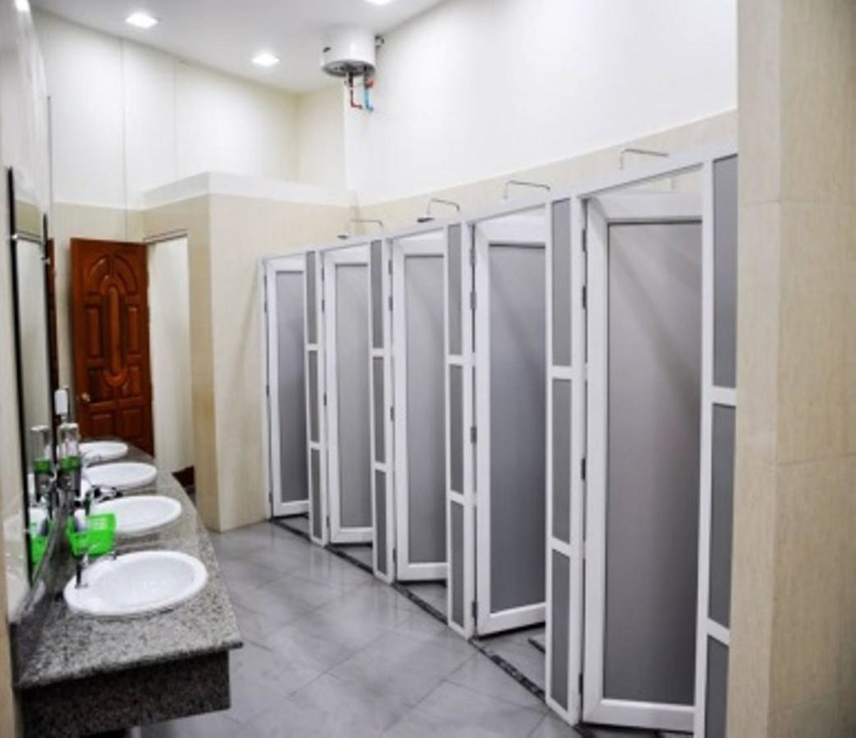 A row of white toilet stalls with a mirror and sinks on the left.