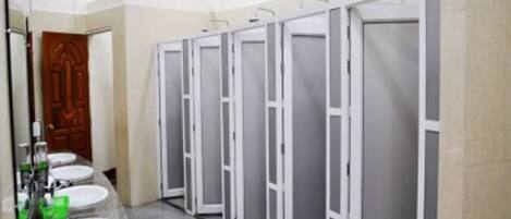 Une rangée de toilettes blanches, avec un miroir et des lavabos sur le côté gauche.