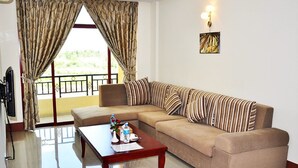 A living room with a beige sofa, striped pillows, a wooden coffee table, and a painting on the wall. - Rose Land Apartment Hotel (Naypyidaw)