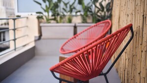 Twee rode geweven stoelen op een balkon met een bamboe muur en potplanten op de achtergrond.
