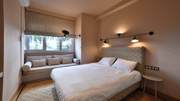 Een slaapkamer met een groot bed, een raamzitje met kussens en wandlampen.