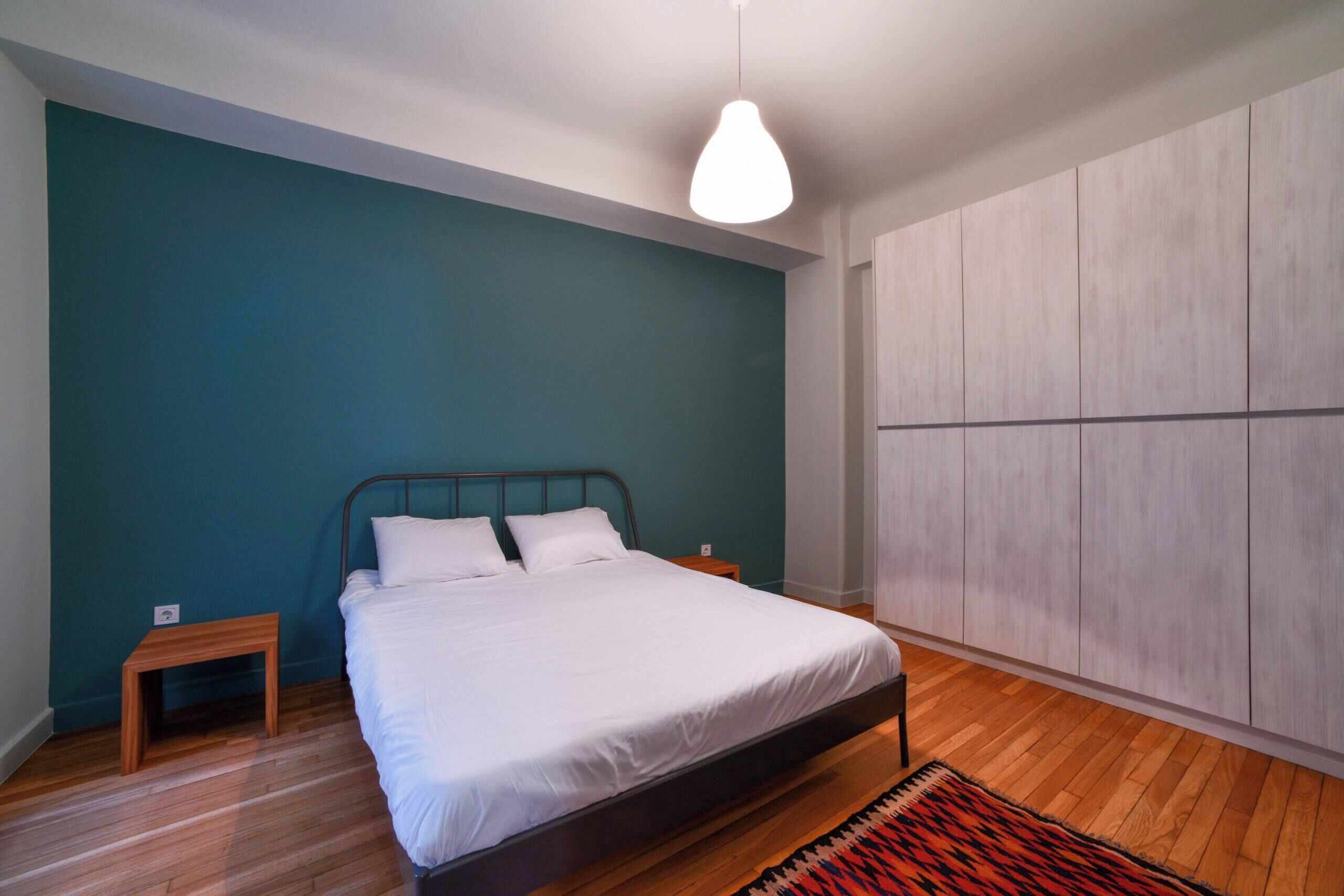 Une chambre moderne avec un lit, un plancher en bois, un mur de couleur turquoise et une armoire.