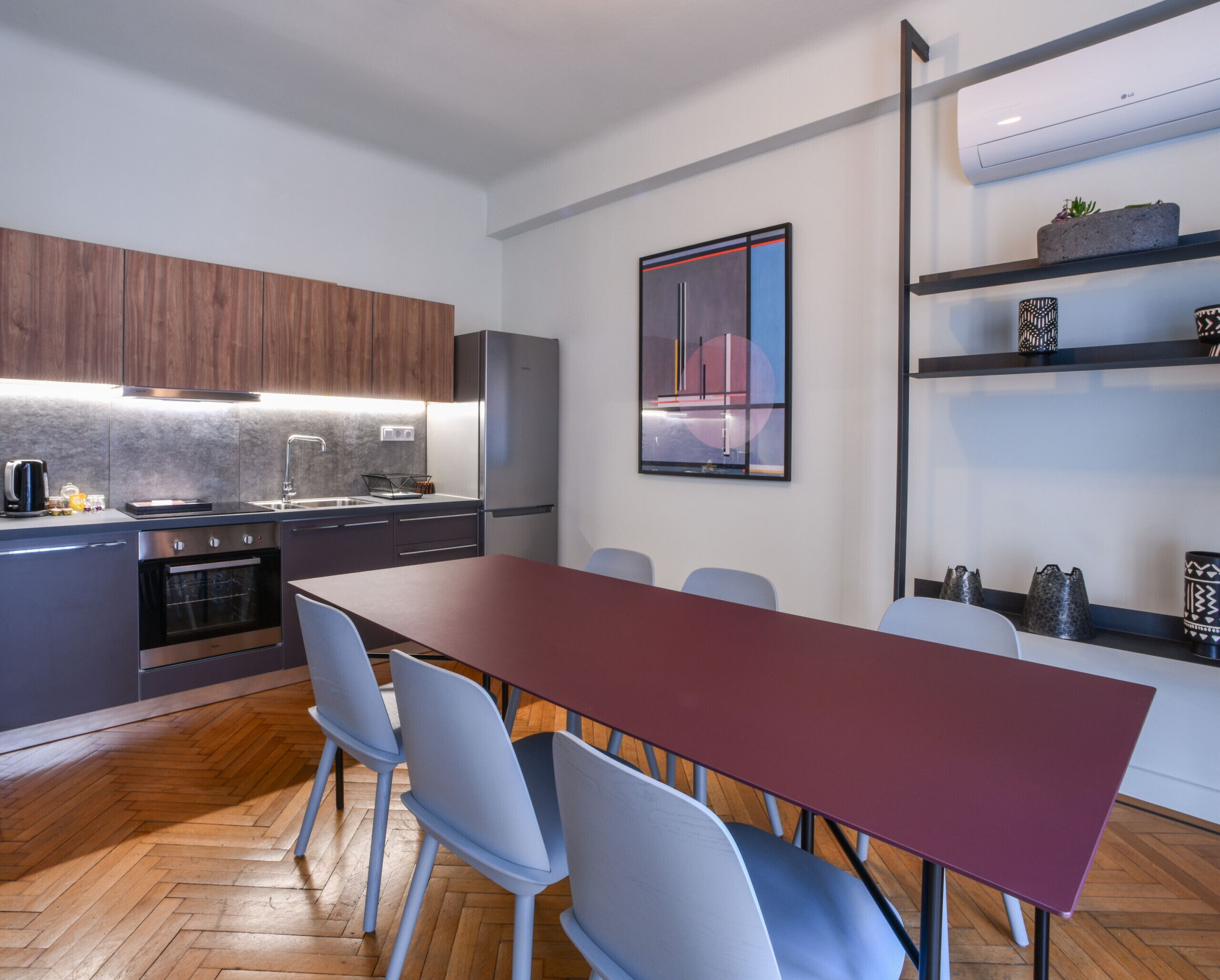 Een moderne keuken met een eethoek, met een lange tafel en stoelen, een inbouwoven en een koelkast.