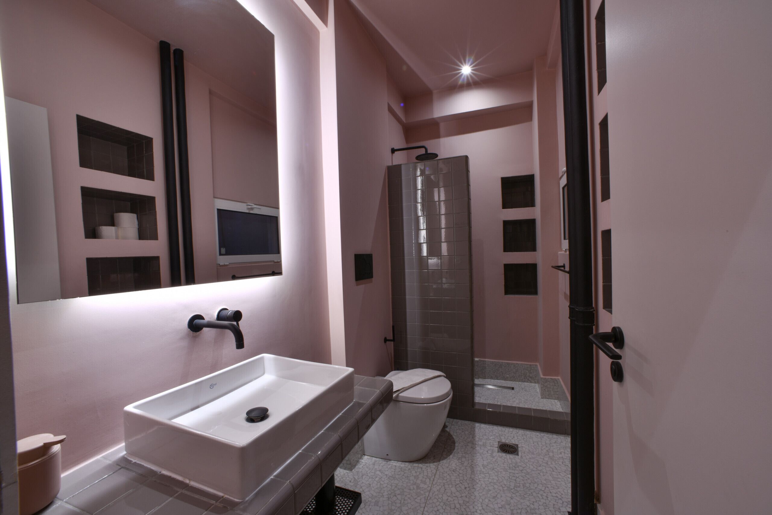 A modern bathroom with a large mirror, a white sink, a toilet, and a glass shower enclosure.