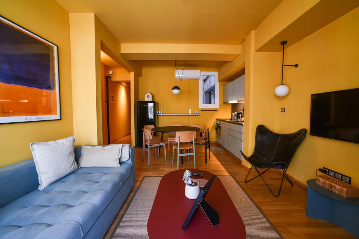 Een moderne woonkamer met een blauwe bank, een rode salontafel en een eethoek met tafel en stoelen.