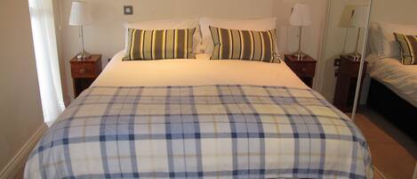 A neatly made bed with a plaid bedspread, two bedside tables with lamps, and a mirror on the wall.