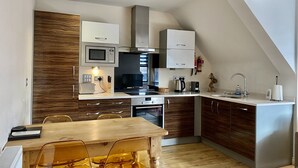 A modern kitchen with white cabinets, a wooden accent wall, and a dining area with a wooden table and yellow chairs. - Churchill Apartments (York)