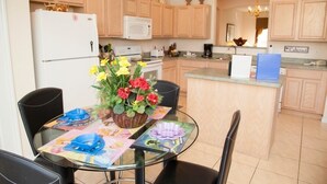 Una cocina con armarios de madera, un refrigerador, microondas y un comedor con mesa y sillas de vidrio.