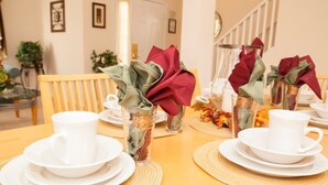 Una mesa de comedor dispuesta con platos blancos, tazas y servilletas atadas con cintas rojas y verdes.