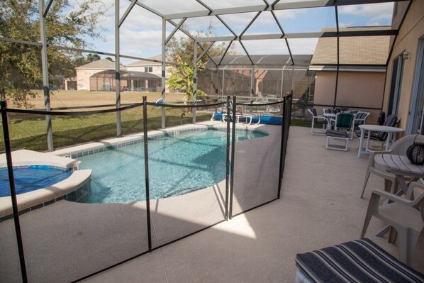 A covered outdoor swimming pool with a hot tub, surrounded by a safety fence. There are lounge chairs and a table on the right side. - Ly53791 - Emerald Island - 6 Bed 5 Baths Villa (Kissimmee)