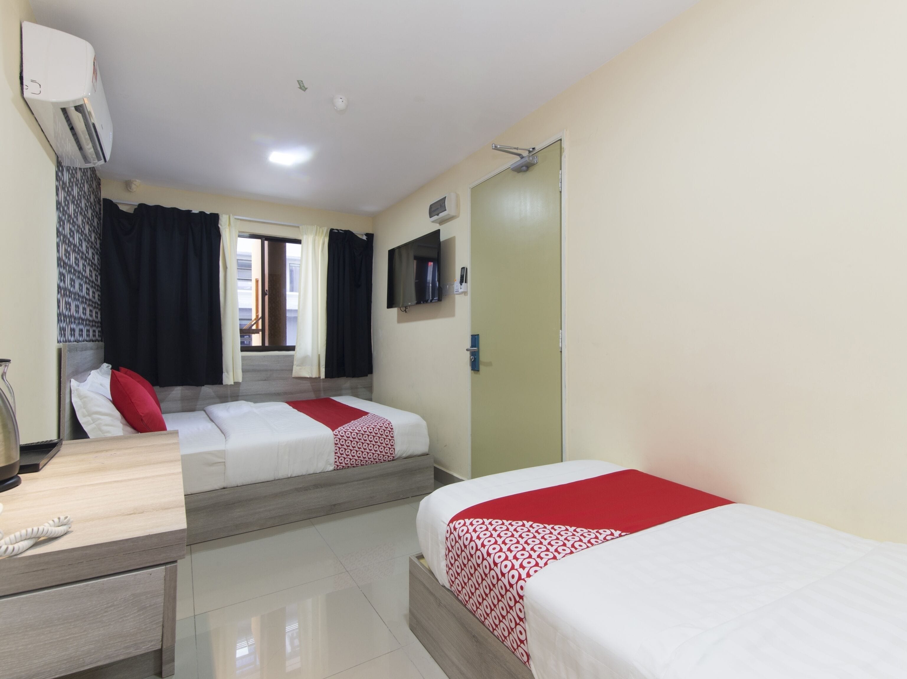 A hotel room with two beds, a desk, a TV, and a door.