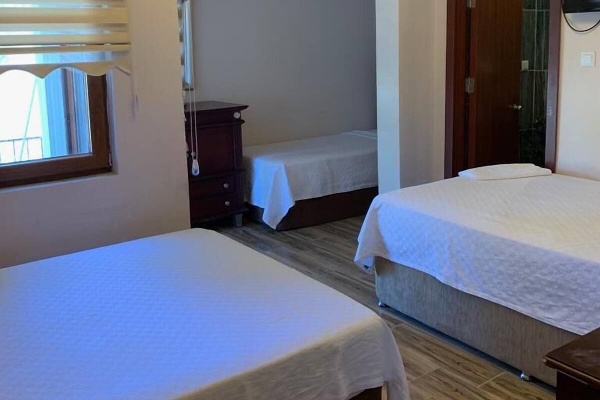 Una camera d'albergo con due letti singoli, pavimento in legno, un armadio, una televisione a muro e una finestra con tende.