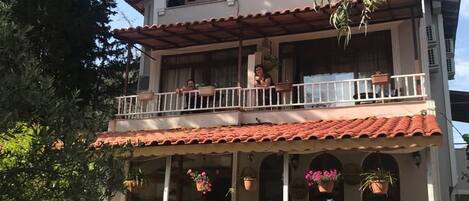 Un edificio de dos pisos con balcones, fachada de tejas y macetas colgantes de flores.