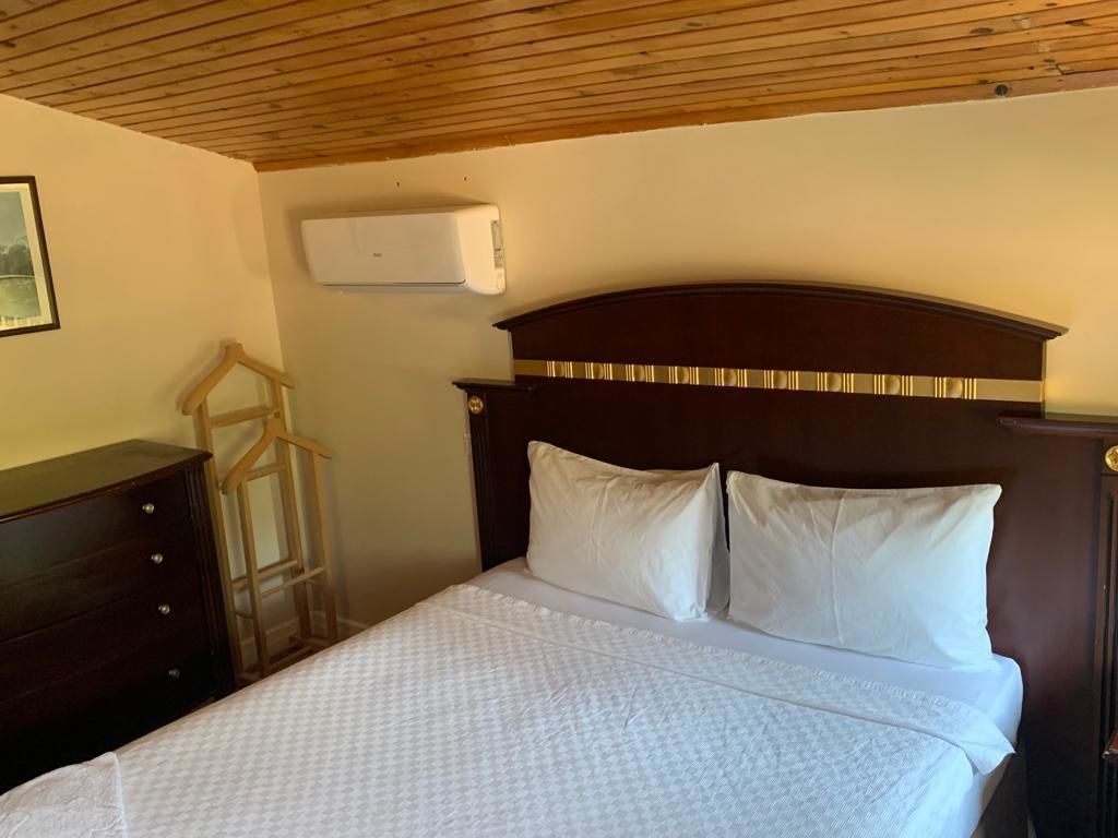 A bedroom with a wooden headboard, a bed with white bedding, a dresser, and a wall-mounted air conditioning unit.