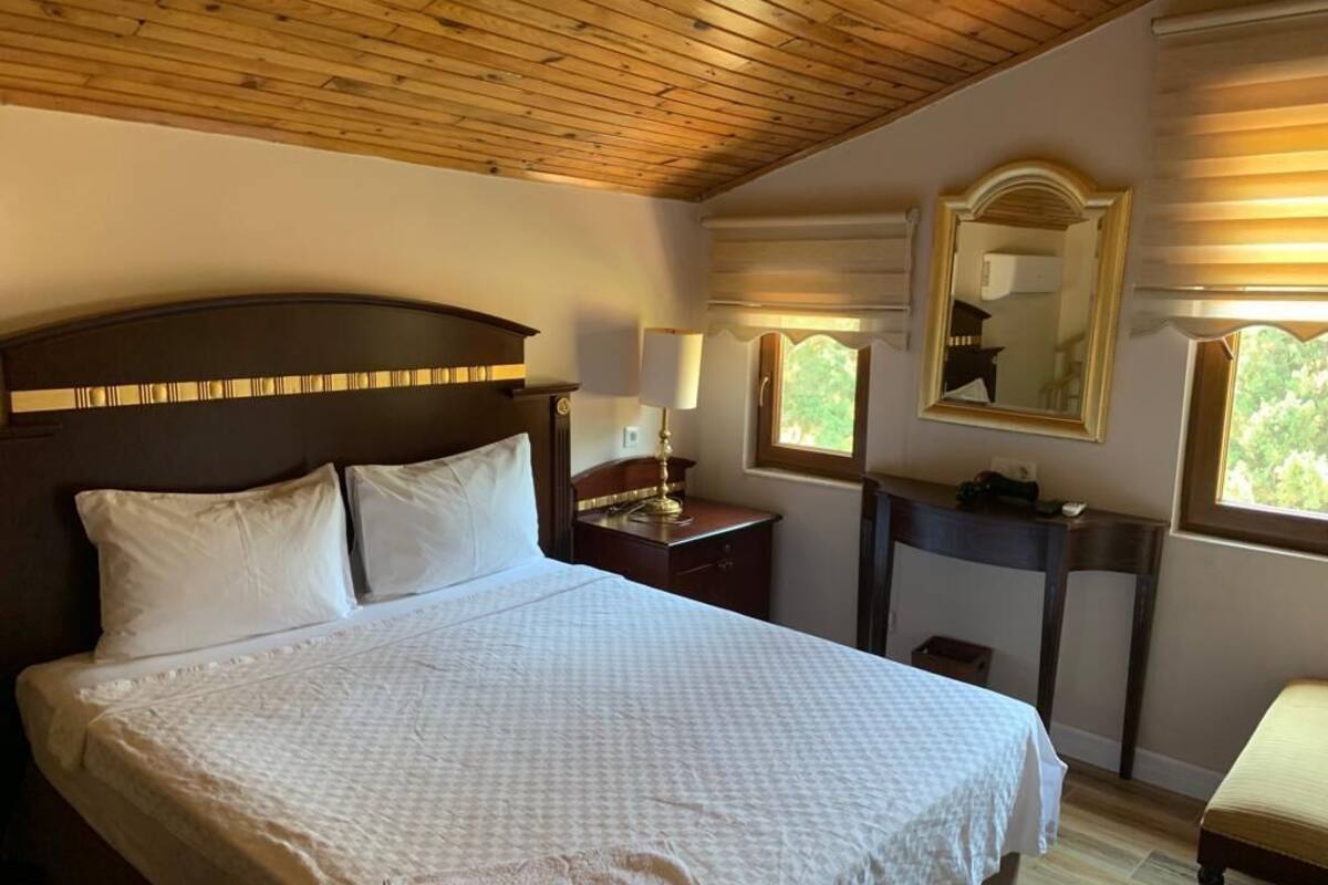 Una camera da letto con un letto grande, soffitto in legno, un comodino con una lampada, uno specchio e una finestra con persiane.