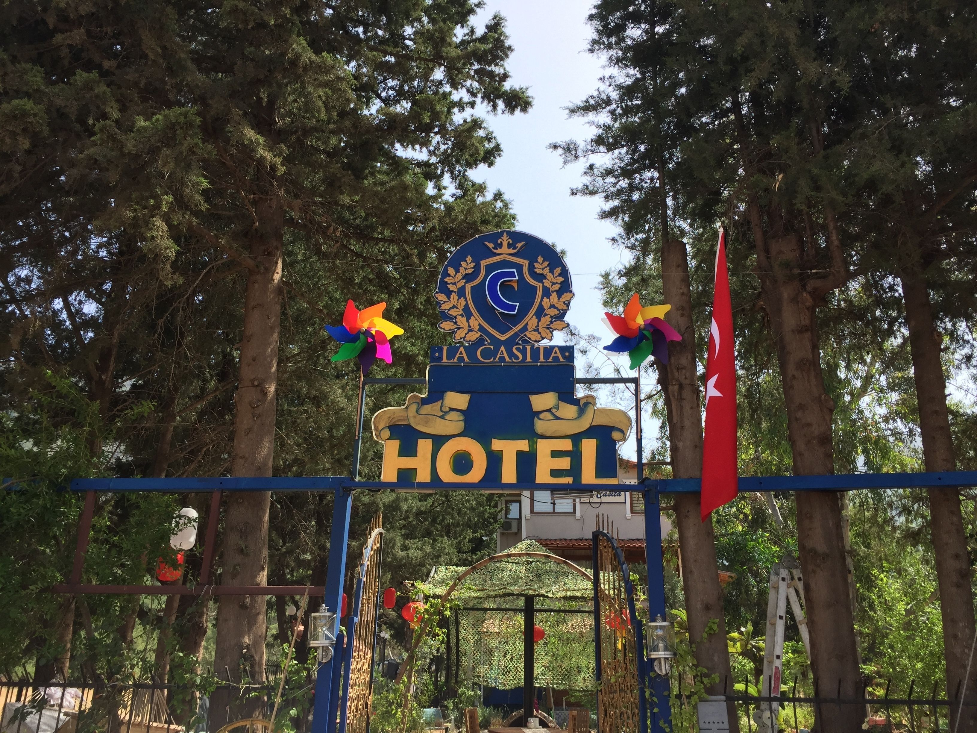 Een bordje voor Hotel La Casita met een blauw en gouden embleem, omringd door bomen en een decoratieve poort.