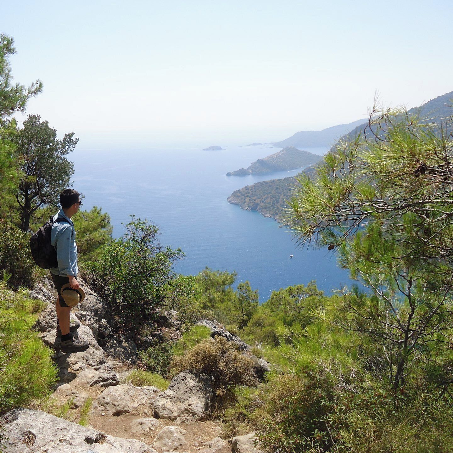 A hiker on a rocky path overlooking a coastal landscape with clear skies.
