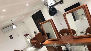 A modern salon with multiple treatment chairs, a wooden reception desk, and large mirrors. - JLW Hostel (Berekuso)