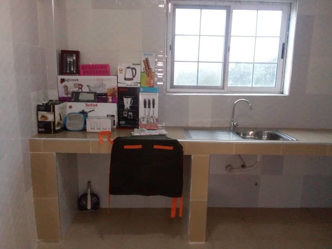Una cocina con ventana, un lavamanos y diversos electrodomésticos y objetos sobre la encimera.