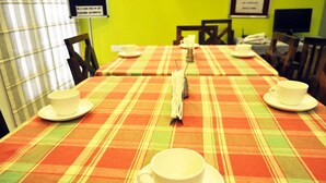 A dining area with tables covered by plaid tablecloths, each with a white cup and saucer. - OYO Premium Saket Metro Station (New Delhi)