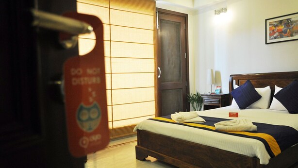 A hotel room with a bed, a wooden door, a nightstand, and a wall-mounted picture. - OYO Premium Saket Metro Station (New Delhi)