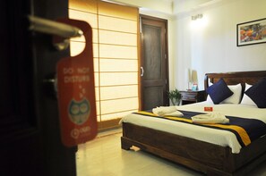 A hotel room with a bed, a wooden door, a nightstand, and a wall-mounted picture.