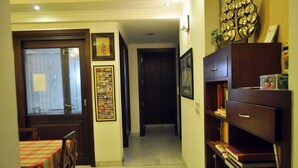 A hallway with a wooden door, a framed poster on the wall, and a bookshelf with books and a canister. - OYO Premium Saket Metro Station (New Delhi)