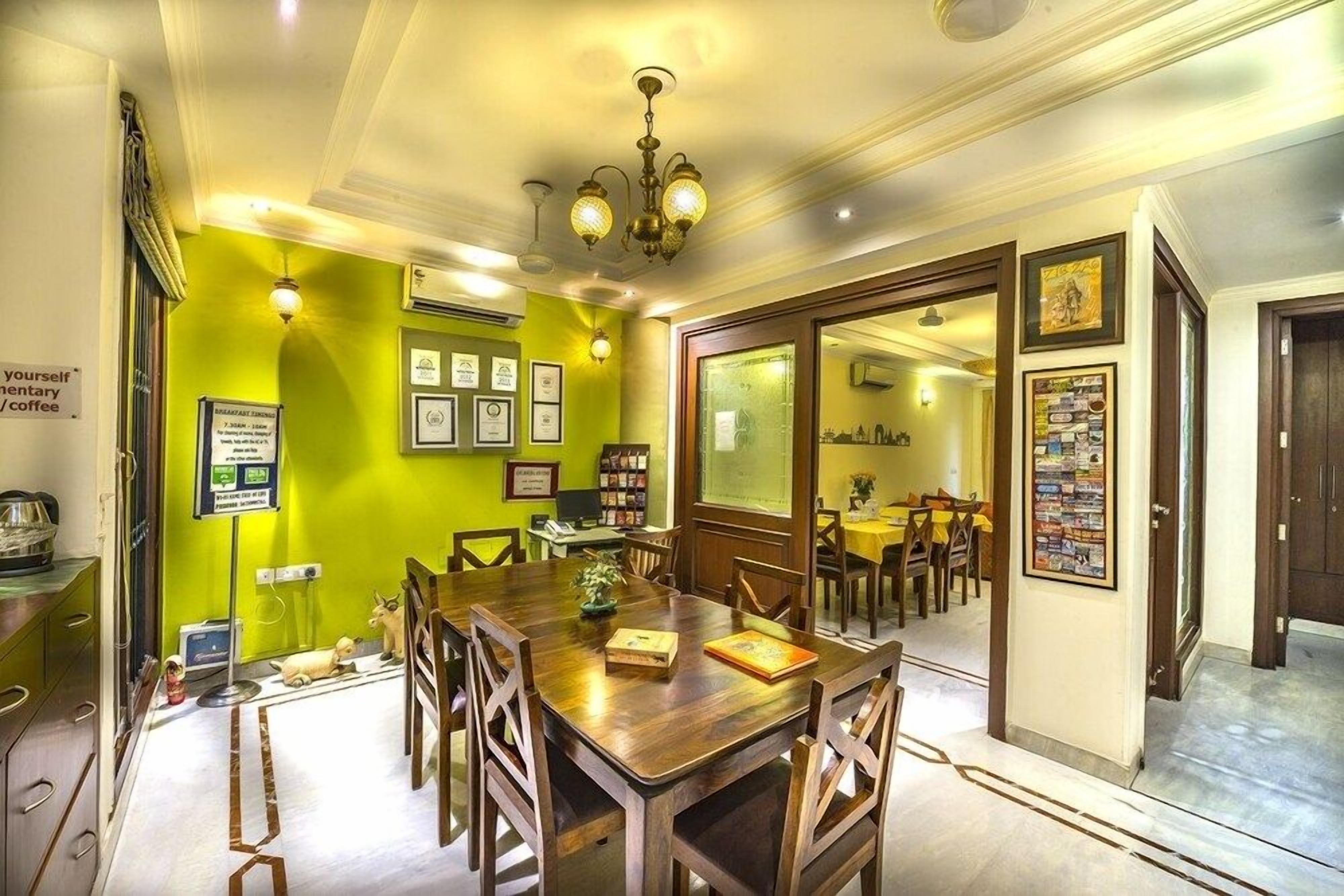 A dining area with a long wooden table, chairs, and a chandelier. There are framed pictures on the walls and a sign indicating breakfast availability.
