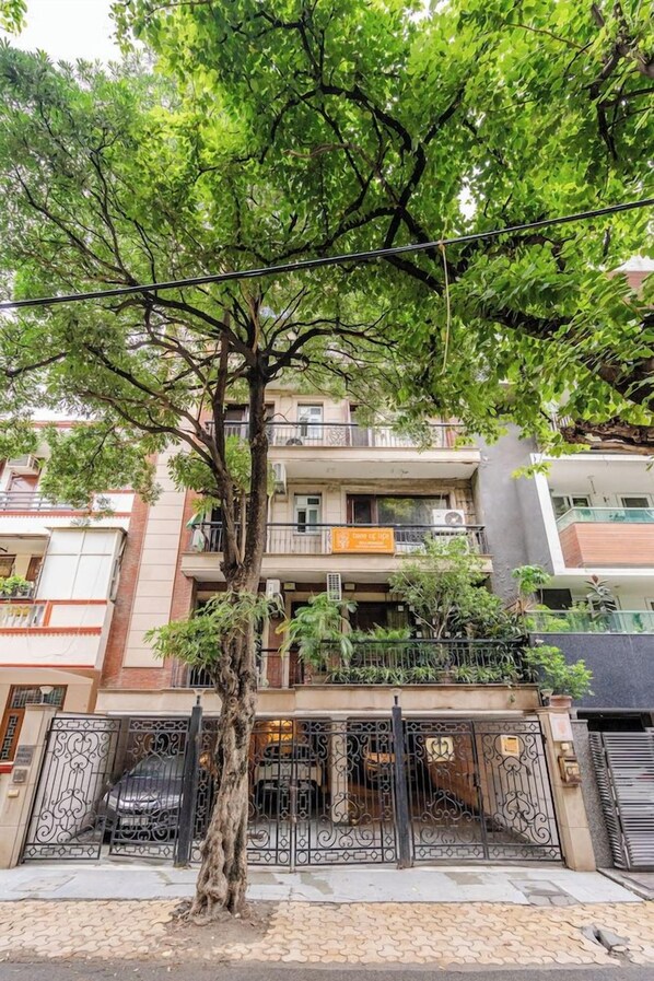 A multi-story residential building with a tree in front, a gated entrance, and balconies on the upper floors.