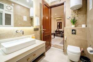 A bathroom with a large sink, toilet, and shower. There is a mirror above the sink and a plant on the wall.