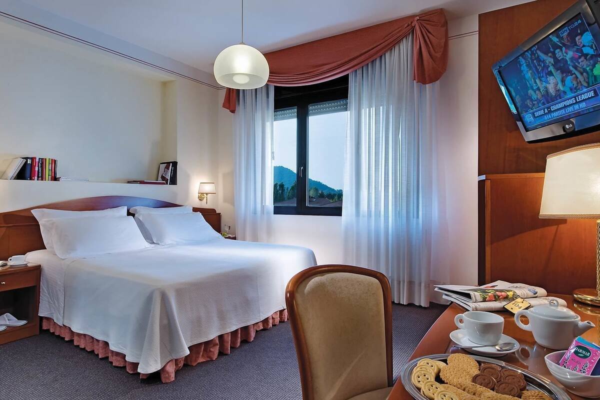 Een hotelkamer met een bed, een bureau met lamp, een stoel, een televisie en een raam met gordijnen.