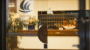 Een hotel receptie met glazen deur, een receptiebalie en een bloempot.