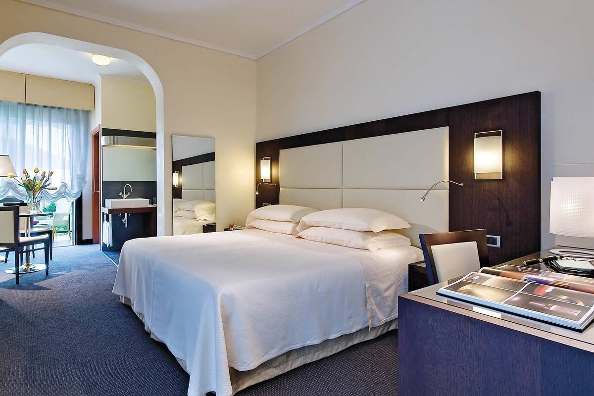 Hotelkamer met een groot bed, een bureau met lamp, een televisie en een badkamer met spiegel en wastafel.